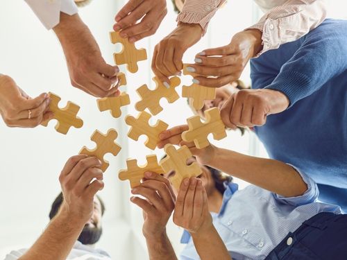 Aumenta la produttività e la coesione del tuo gruppo di lavoro con i nostri consigli sul team building! Persone tengono pezzi di puzzle in mano